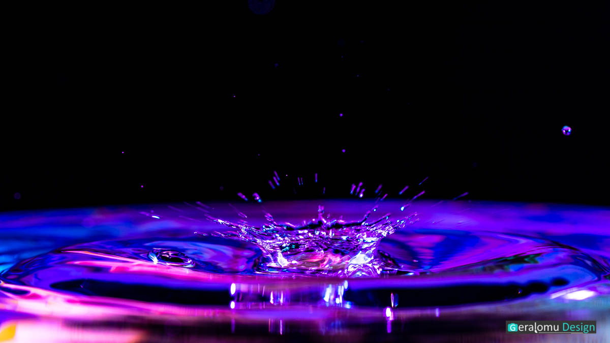 Makro Wassertropfenfotografie: Blau- und lilafarbige, kronenförmige Wasserfontäne auf die Wasseroberfläche