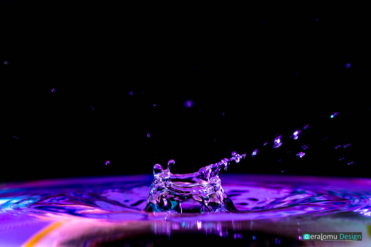 Makro Wassertropfenfotografie: Blau- und lilafarbige Wassersäule über der Wasseroberfläche