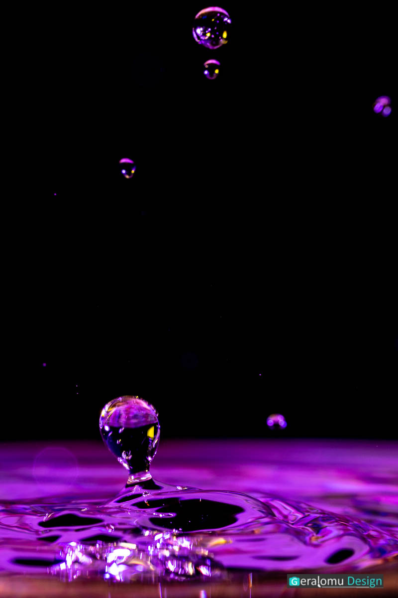 Makro Wassertropfenfotografie: Lilafarbige schwebende Kugeln über der Wasseroberfläche