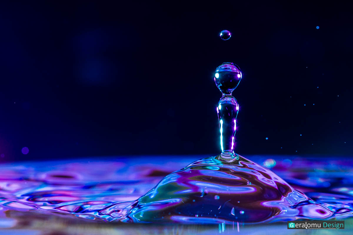 Wassertropfenfotografie Makro: Blau- und lilafarbige Wassertropfensäule nach dem Aufprall eines Wassertropfens auf der Wasseroberfläche