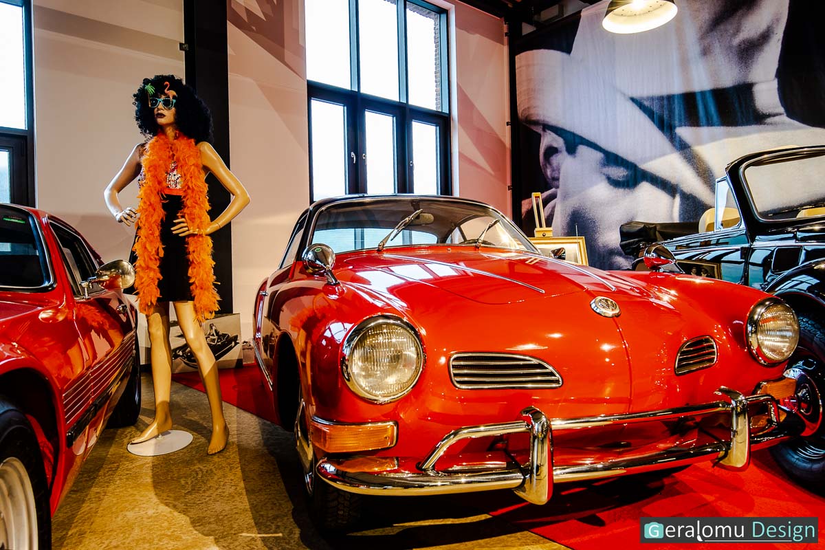 Wir sehen ein rotes VW-Karmann-Ghia-Sportcoupé mit einer seitlich daneben stehenden Schaufensterpuppe in flippiger Kleidung der damaligen Zeit im Zylinderhaus in Bernkastel-Kues.